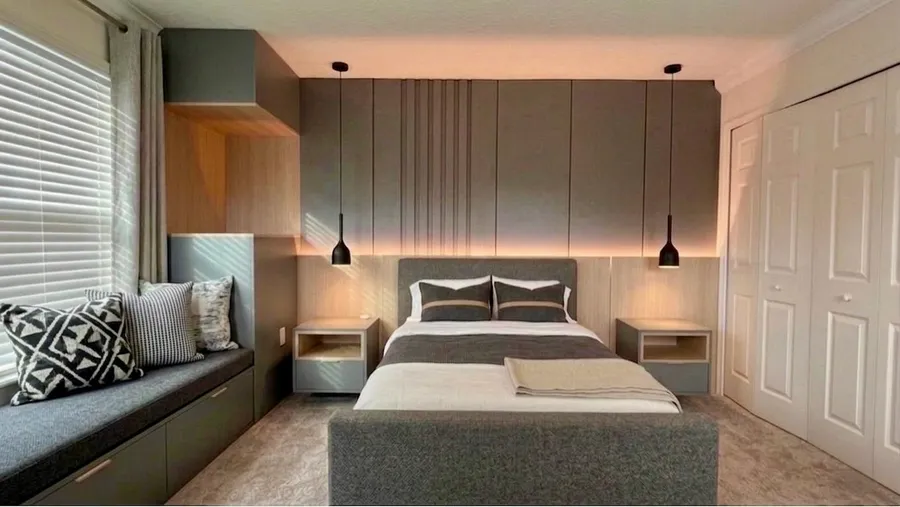 Bedroom with a gray paneled feature wall, integrated headboard, floating nightstands, pendant lights, and a window seat