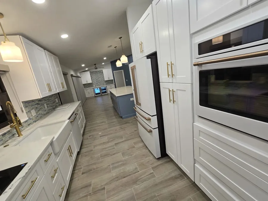 White shaker kitchen with brass hardware, farmhouse sink, wall ovens, and a blue island by CoreBuild